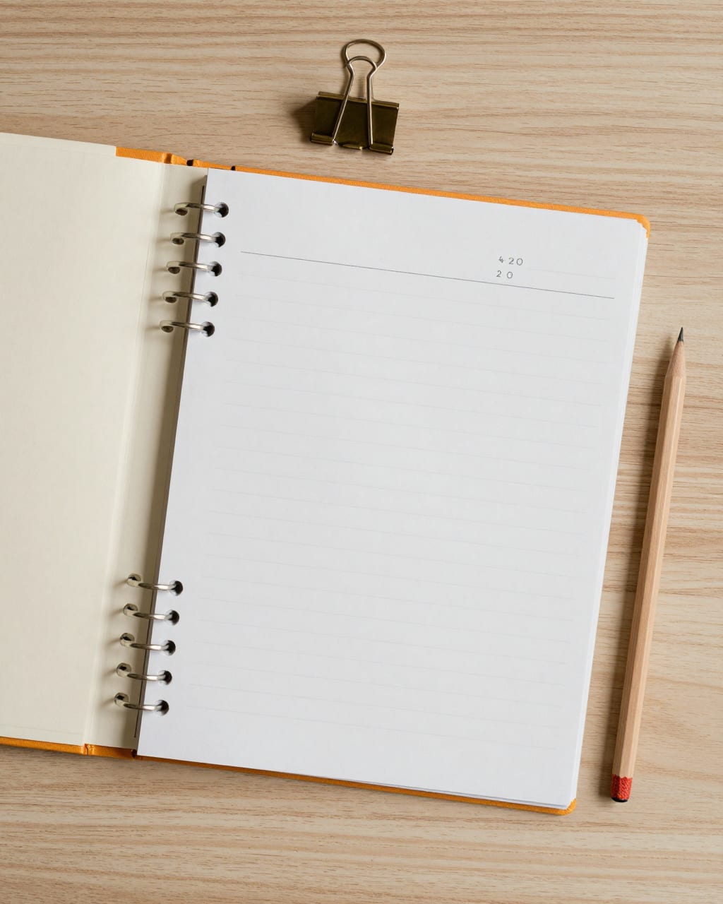 An open ruled notebook, a binder clip and a pencil on an oak desk